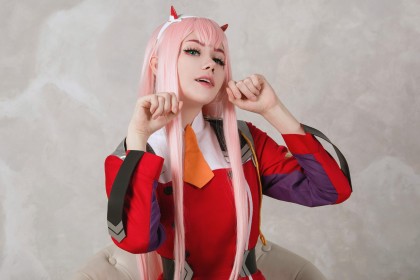 anastasia komori,caucasien,cheveux rose,cornes,cosplay,darling in the franxx,femme,frange,pose féline,sourire,uniforme,yeux bleu,zero two