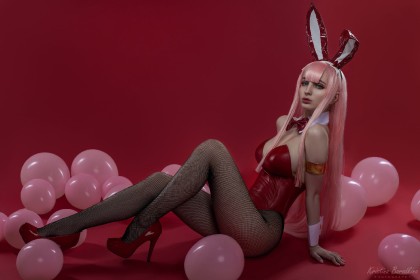 assis,background rouge,ballon,caucasien,cheveux rose,collant,collant en résille,cosplay,costume de lapin,darling in the franxx,fausses oreilles animaux,femme,frange,hologana,jambes,leotard,noeud papillon,résille,talon aiguille,très long cheveux,yeux turquoise,zero two